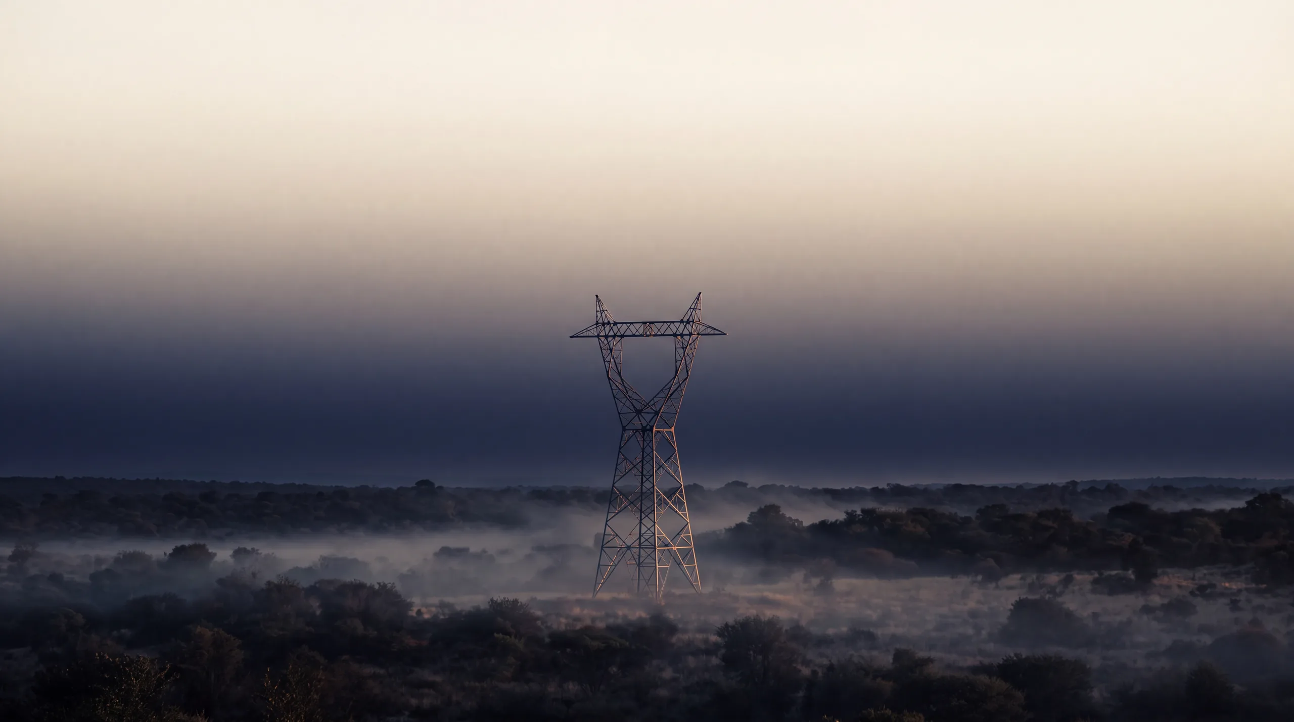Solitary transmission tower at dawn in open savanna, mist at its base